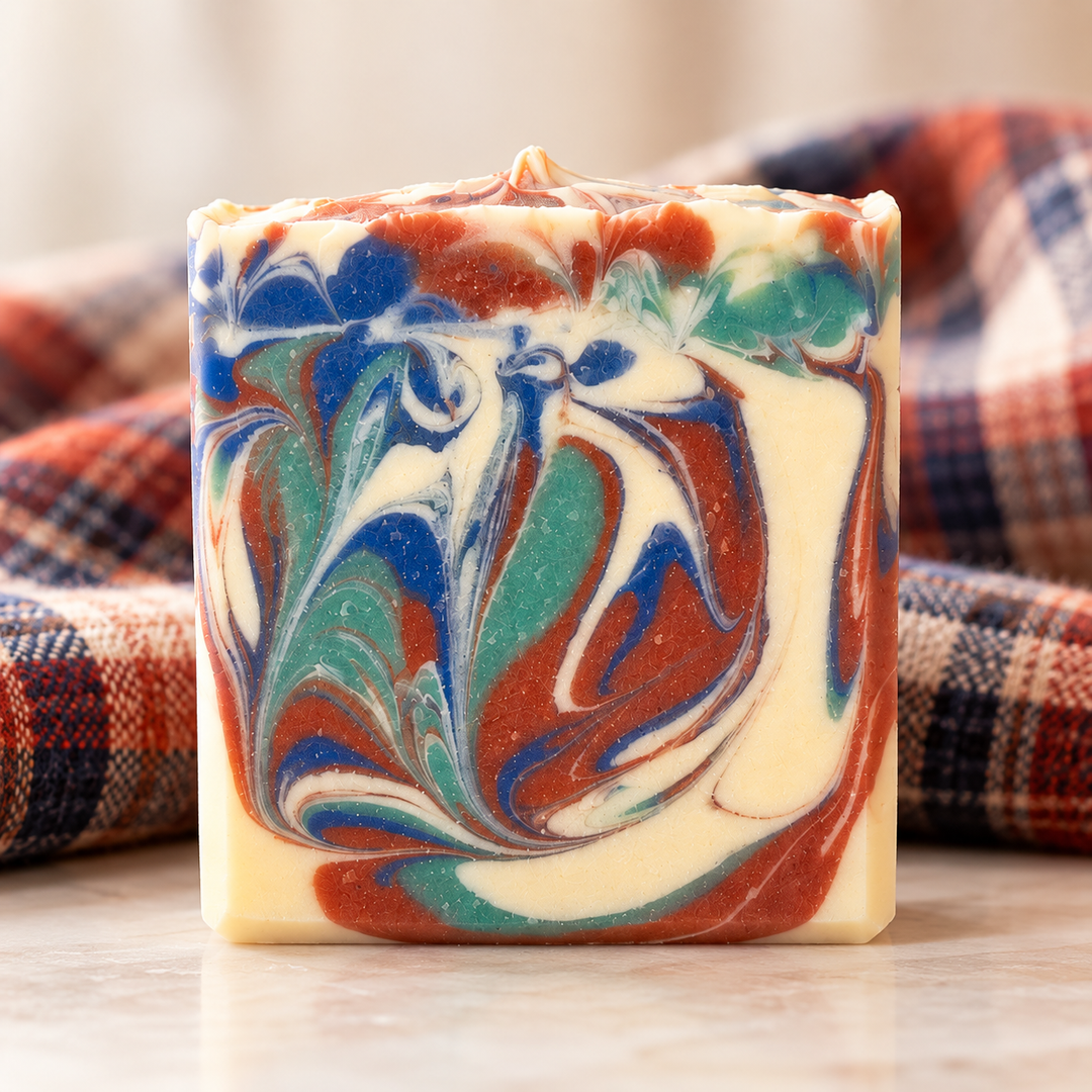 Handmade Cozy Flannel goat milk soap by Always Bubbles, featuring beautiful swirls of deep blue, teal green, rust orange, and creamy ivory, photographed against a softly blurred flannel fabric background.