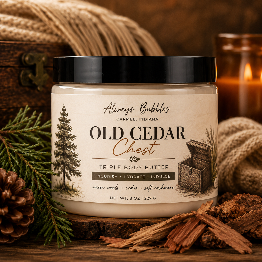 Always Bubbles Old Cedar Chest Triple Body Butter in a clear jar with a black lid, styled with a vintage cedar chest, cozy knit blanket, cedar wood, evergreen branches, and warm candlelight.