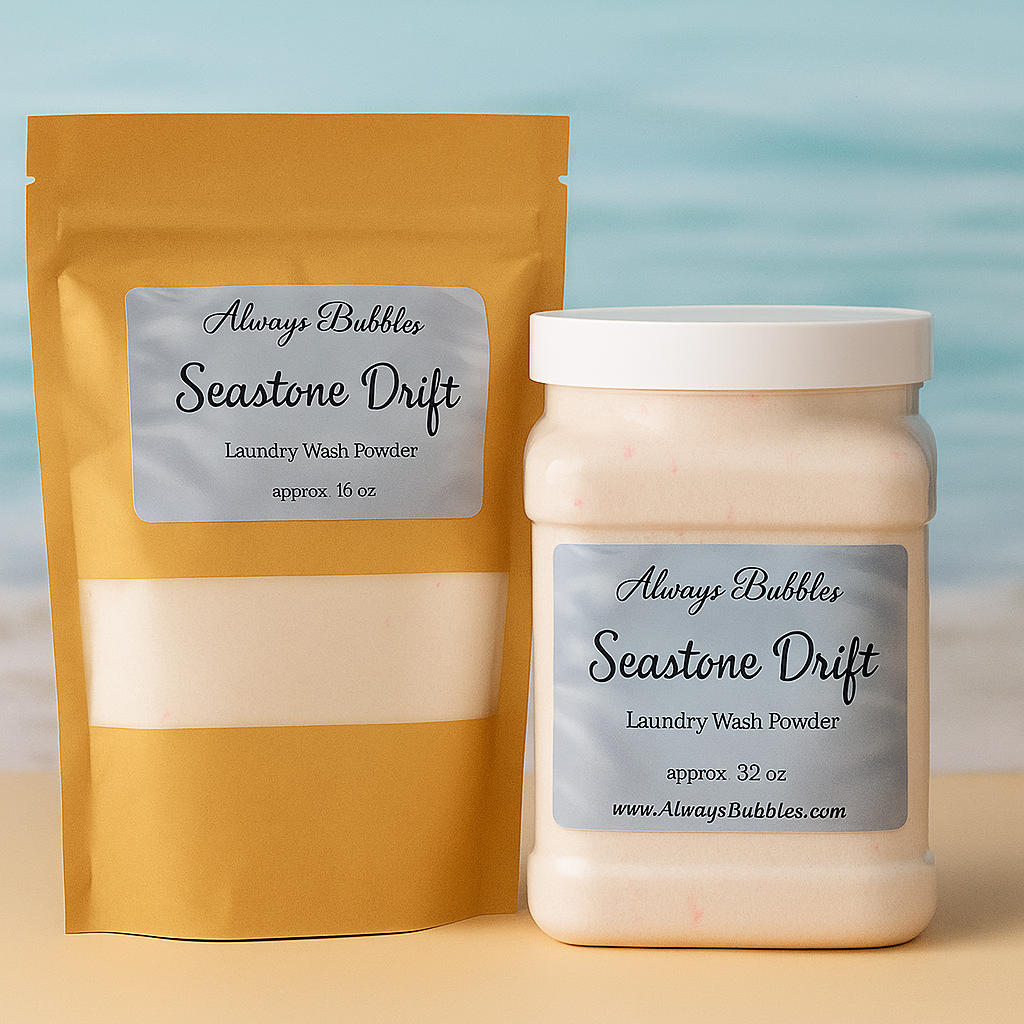 Always Bubbles Seastone Drift Laundry Wash Powder in 32 oz jar and 16 oz kraft refill bag, displayed against a soft ocean-inspired background. Coastal blue and sand tones evoke the fresh, clean scent of Seastone Drift.